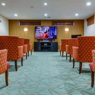 A small theater room with rows of upholstered chairs facing a large television screen.