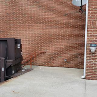 A view of a brick wall with a dumpster and a small access ramp.