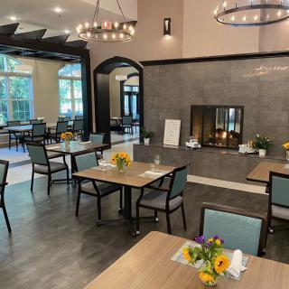 A cozy dining area with neatly arranged tables and chairs, featuring a central fireplace and elegant lighting.