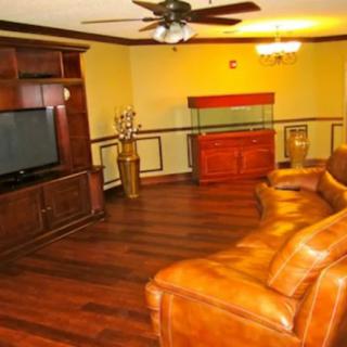 A cozy living room featuring a brown leather sofa, wooden entertainment center with a large TV, and elegant wood flooring.