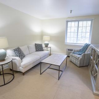 A cozy living room with a sofa, coffee table, armchair, and two lamps by the window.