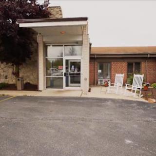A welcoming entrance to a building with rocking chairs on the porch and landscaped surroundings.