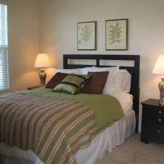 A cozy bedroom with a neatly made bed, decorative pillows, bedside lamps, and wall art.