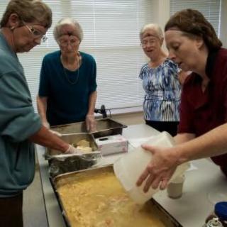 Volunteers preparing food in a community kitchen setting.