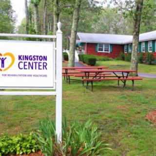 A sign for Kingston Center stands in front of a building surrounded by trees and picnic tables.