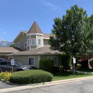 A residential house with a pointed roof, surrounded by trees and bushes on a sunny day.