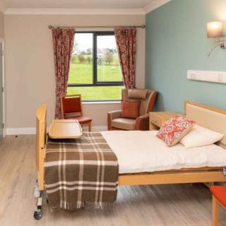 A cozy hospital bedroom with a single bed, armchair, and large window.