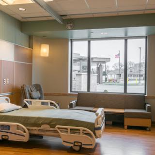 A modern hospital patient room featuring a bed, comfortable seating, and large windows for natural light.