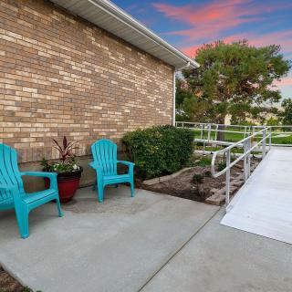 Outdoor seating area with teal chairs next to a brick building and a ramp.
