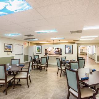 A spacious dining area with neatly arranged tables and chairs, featuring artwork on the walls and ceiling lights.