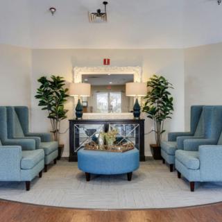 A stylish lobby with blue armchairs arranged around a central table, complemented by plants and decorative lamps.