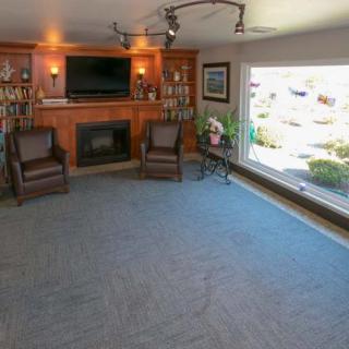 A cozy living room featuring a fireplace and television, with bookshelves and armchairs alongside a large window.