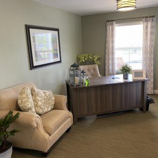 A cozy office space with a desk, chair, and sofa, complemented by plants and a window.