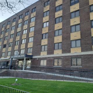 A multi-story brick apartment building featuring numerous windows and a grassy area in front.