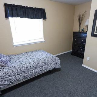 A simple bedroom with a single bed, black curtains, and a dresser against beige walls.