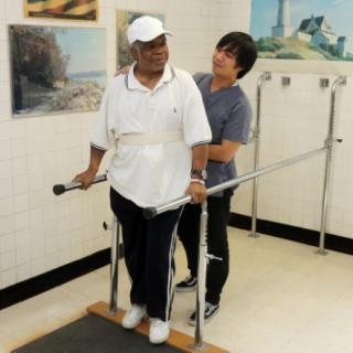 A therapist assists a patient during a physical therapy session using parallel bars.