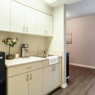 A modern kitchen area with white cabinets, a sink, and wood flooring.