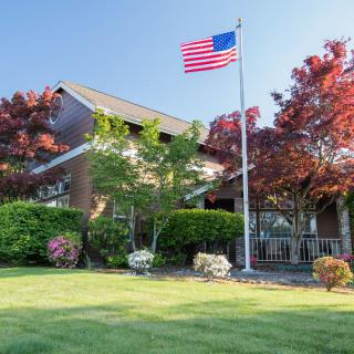 A suburban house with an American flag flying in the yard, surrounded by a well-maintained garden and trees.