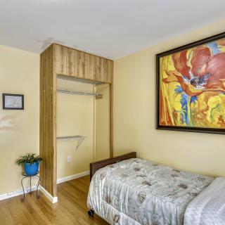 A cozy bedroom with a single bed, colorful artwork on the wall, and a small plant near an open closet.