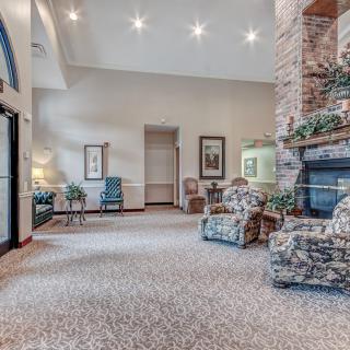 A spacious living room with a stone fireplace, comfortable armchairs, and decorative plants.