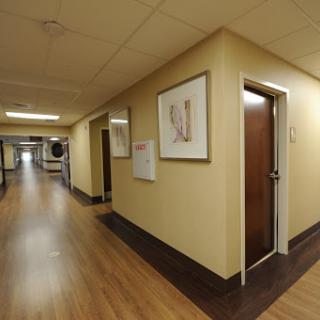 A view of a hospital corridor featuring a door and framed artwork on the wall.