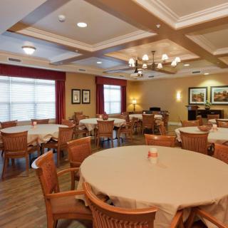 A cozy dining room with round tables and wooden chairs, decorated with a chandelier and framed artwork on the walls.