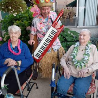 A lively scene with seniors enjoying a tropical-themed gathering, featuring leis and music in a garden setting.