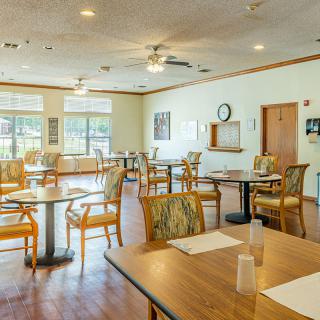 A spacious dining room with wooden tables and chairs, well-lit by natural light.