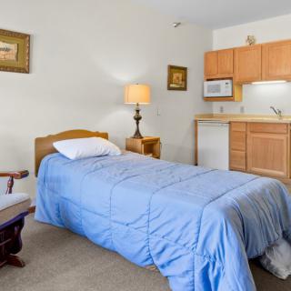 A cozy bedroom with a single bed, blue bedding, and a kitchenette in the corner.