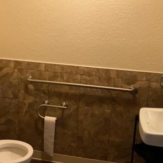A bathroom with a toilet, a sink, and a handrail against a tiled wall.
