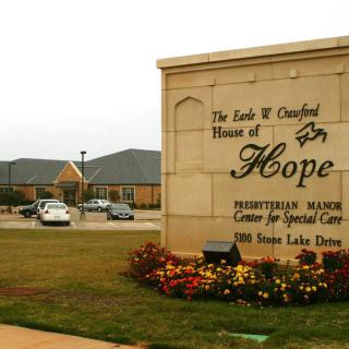 The exterior sign of the House of Hope, a care facility surrounded by landscaped grounds and flowers.