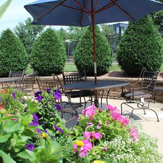 A serene outdoor patio with a table and chairs surrounded by vibrant flowers and greenery.