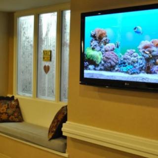 A cozy living room featuring a wall-mounted TV displaying an aquarium scene next to a window seat with pillows.