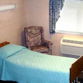 A simple hospital room with a bed, chair, and window with an air conditioner.