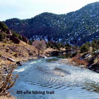 A scenic off-site hiking trail running alongside a river with mountainous landscape in the background.