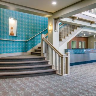 A cozy hotel lobby featuring a staircase with carpeted steps and patterned wallpaper, complemented by decorative artwork on the wall.