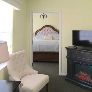 A cozy bedroom with a TV and fireplace, featuring a plush chair and a bed with an ornate headboard.