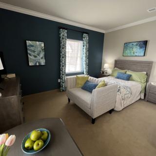 A cozy bedroom interior featuring a bed with decorative pillows, a small sofa, and modern artwork on the walls.