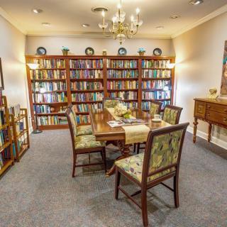 A cozy reading room with a large bookshelf, table, and chairs.