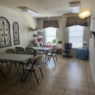 A spacious multi-purpose room with tables and chairs set up for a gathering, featuring natural light from the windows.