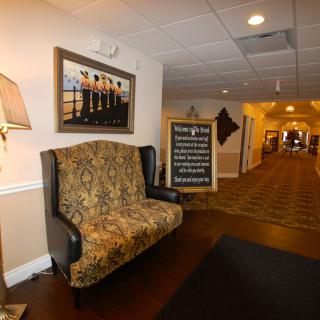 A well-decorated hallway with a patterned sofa, framed artwork, and a lamp, featuring a signboard in front.