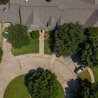 Aerial view of a residential house with a driveway and front yard surrounded by trees.