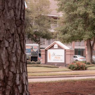 An apartment complex with surrounding trees and a sign near the parking area.
