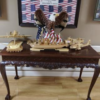 A patriotic display featuring intricately crafted wooden ship models and a majestic eagle sculpture atop a beautifully designed table.
