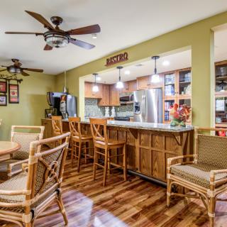 A modern kitchen and dining area featuring wooden flooring, bar stools, ceiling fans, and warm indoor lighting.