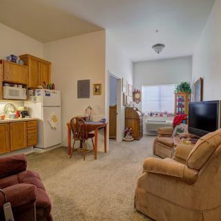 A cozy apartment living space featuring a small kitchen, dining area, and seating with a television.