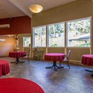 A spacious dining area with round tables covered in red tablecloths and large windows letting in natural light.