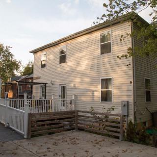 A two-story house with vinyl siding and a wooden deck surrounded by a fence.