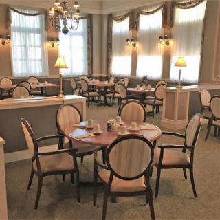 An elegant dining room with neatly arranged tables and chairs, softly lit by lamps.