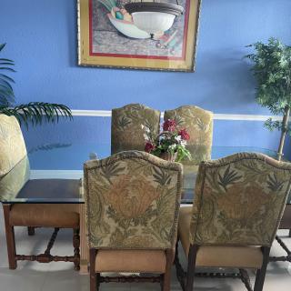 A dining room with an elegant table set, ornate chairs, and decorative elements including a framed painting and indoor plants.